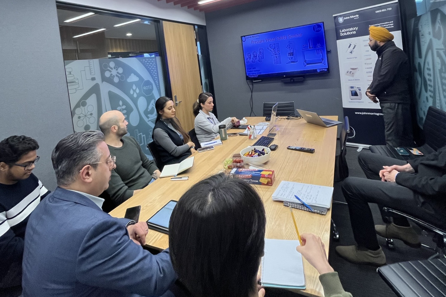 John Morris Group conducting a Pressure Vessel Safety Workshop at the University of Auckland, with Kripan Singh presenting and participants engaging in laboratory safety training on Parr reactors.