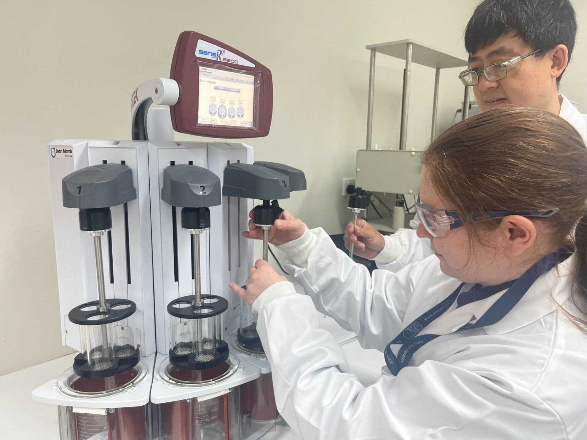 Scientists setting up the Distek sensIR 3200 disintegration system with John Morris Group branding visible