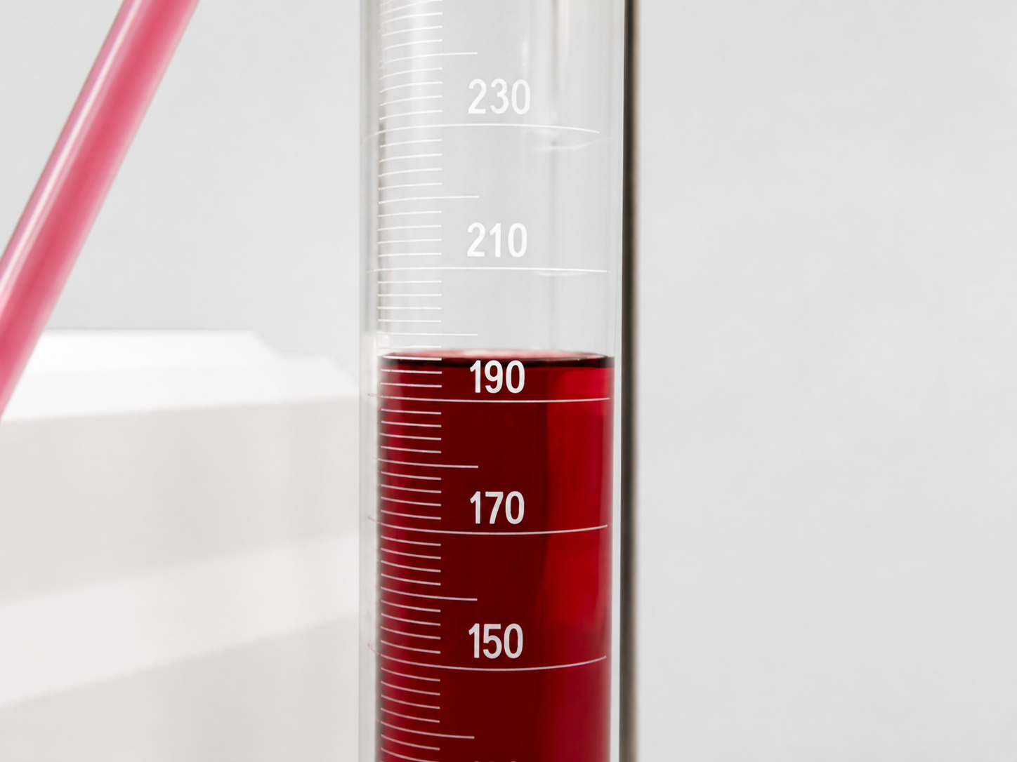 Graduated cylinder showing a red liquid level being read against the millilitre markings after a calibration run